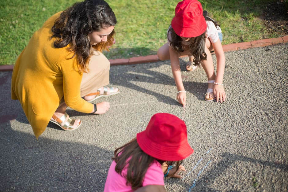 A nanny and two children drawing together on the pavement outdoors in Portugal.