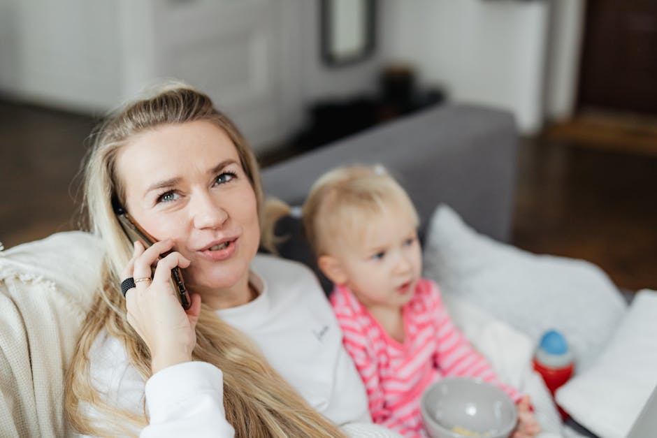 Mother talking on phone while relaxing with her child indoors. Cozy family moment with technology.